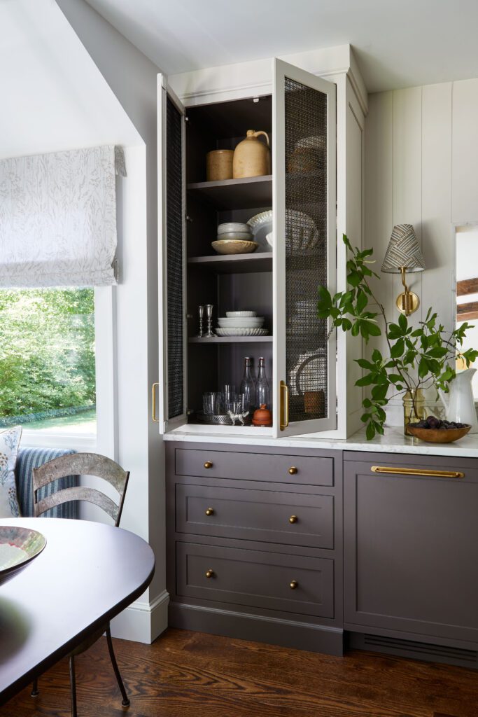 Custom dark gray cabinetry with brass hardware, mesh cabinet doors, marble countertop, and built-in storage by Unique Kitchens & Baths™.