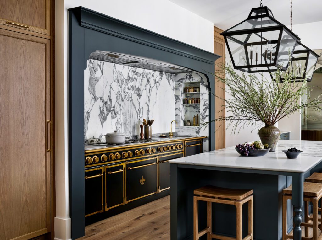 Luxury kitchen with custom natural wood cabinetry, black architectural range surround, dramatic marble backsplash, brass-accented range, and marble island by Unique Kitchens & Baths™.