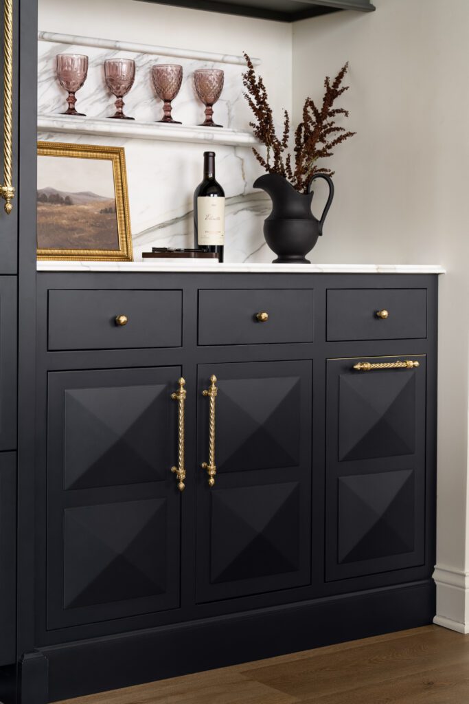 Custom black cabinetry with geometric door detailing, marble backsplash, brass hardware, and built-in display shelving by Unique Kitchens & Baths™.