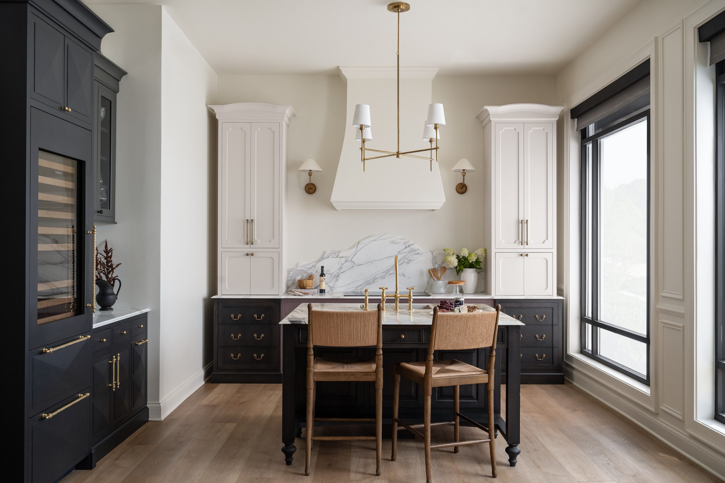Custom black and cream kitchen cabinetry with furniture-style island, marble backsplash, brass hardware, and architectural detailing by Unique Kitchens & Baths™.