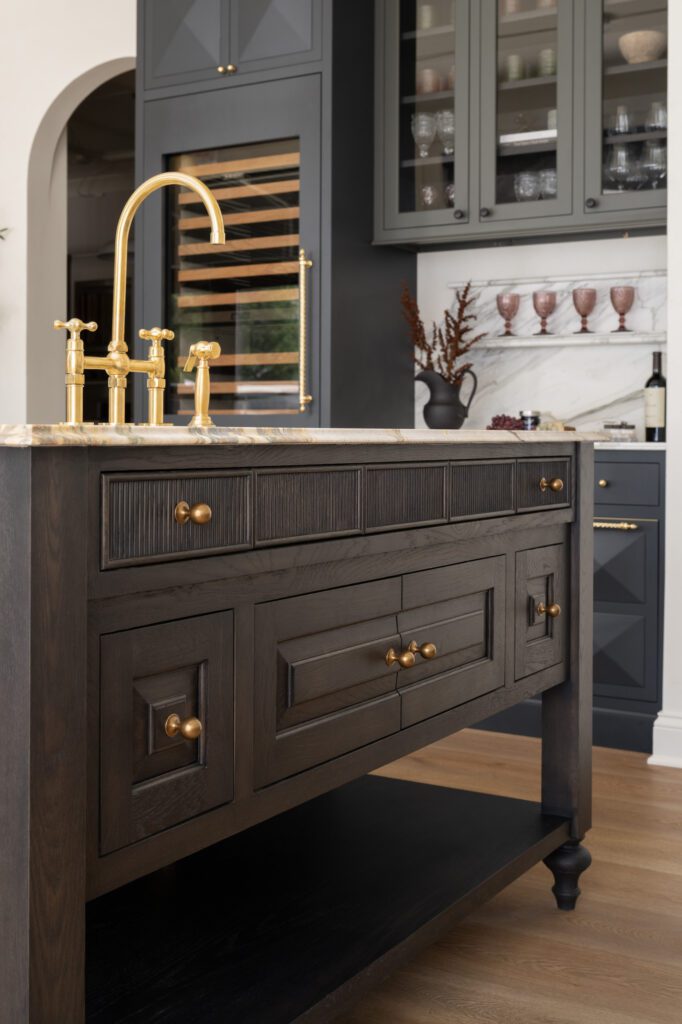 Custom dark wood kitchen island with detailed millwork, brass hardware, marble countertop, and integrated storage by Unique Kitchens & Baths™.