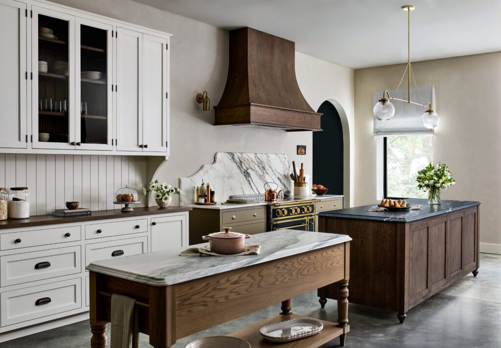 Timeless custom kitchen with white cabinetry, marble countertops, warm wood islands, statement range hood, and brass details by Unique Kitchens & Baths™.