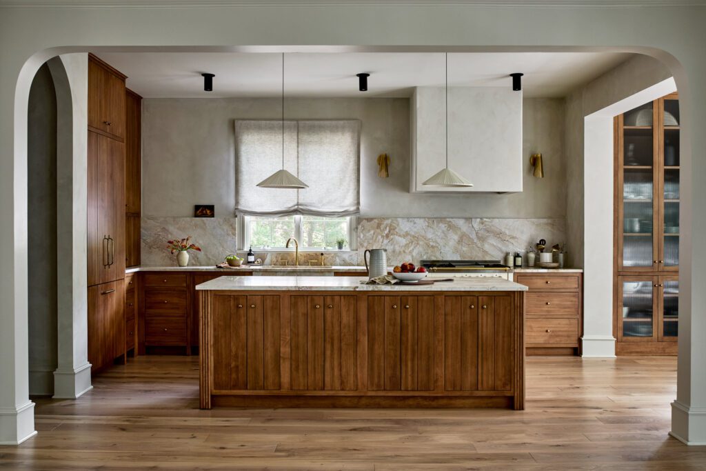 Luxury kitchen with custom natural wood cabinetry, large wood island, stone backsplash, brass fixtures, and arched architectural details by Unique Kitchens & Baths™.