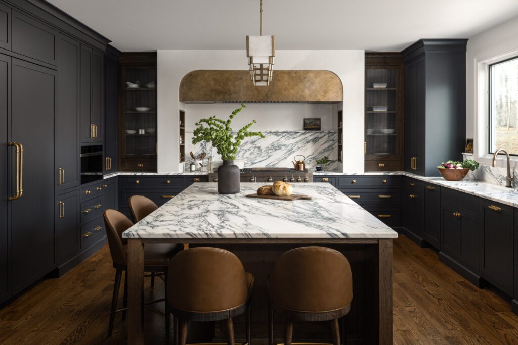 High-end kitchen with custom black cabinetry, brass hardware, dramatic marble countertops and backsplash, and large wood island by Unique Kitchens & Baths™.