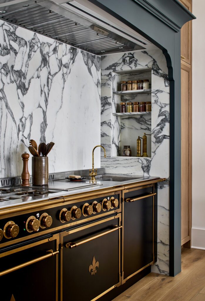 Statement black and brass range framed by dramatic marble slab walls and custom architectural cabinetry by Unique Kitchens & Baths™.